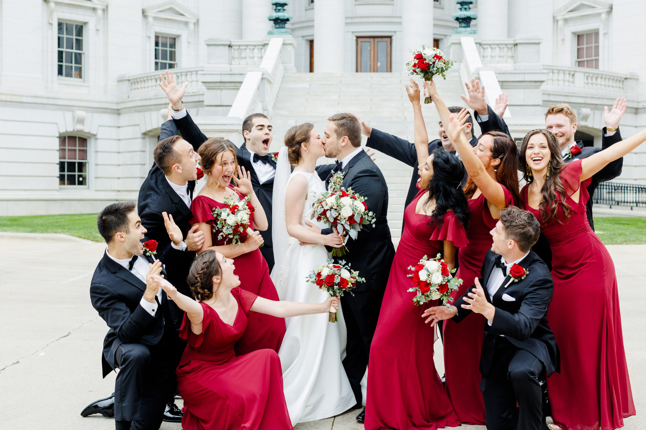 Wedding party cheering while bride and groom kiss in front of the Madison, Wisconsin state capitol