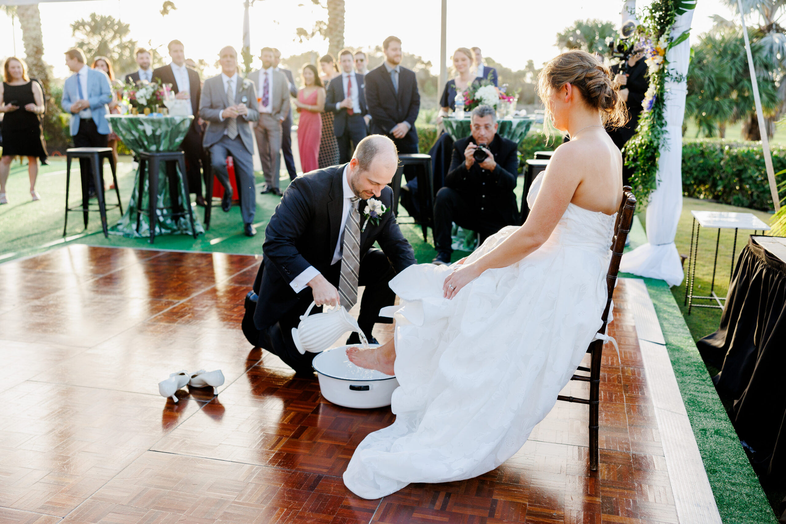 Groom washes the feet of his bride outside during the cocktail hour at their wedding reception, imitating Jesus at the Last Supper.